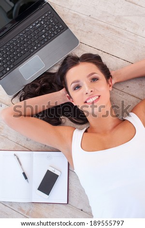 Working at the computer. Top view of beautiful young woman lying on the floor with computer and mobile phone