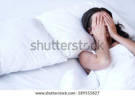Depressed women in bed. Top view of young sad women lying on the bed and hiding her face in hands
