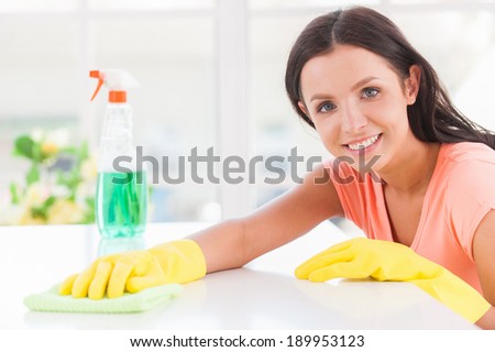 Cheerful housewife. Young beautiful woman yellow gloves leaning at the table and smiling