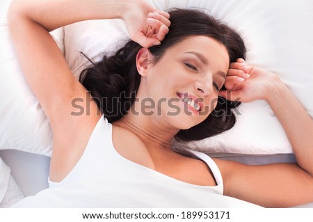 Morning stretching. Beautiful young smiling woman lying in bed and stretching out