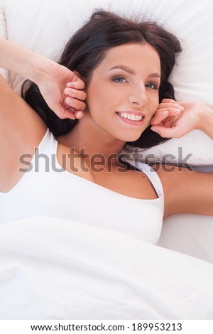 Starting a day from stretching. Beautiful young smiling woman stretching out in bed and looking at camera