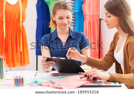 Working on new fashion look together. Two beautiful female designers discussing something while sitting at the working place