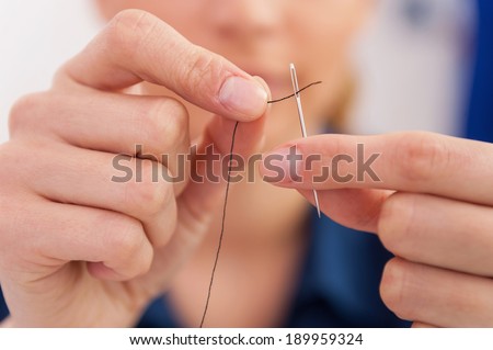 Thread into the needle. Close-up of woman pulling thread into the needle