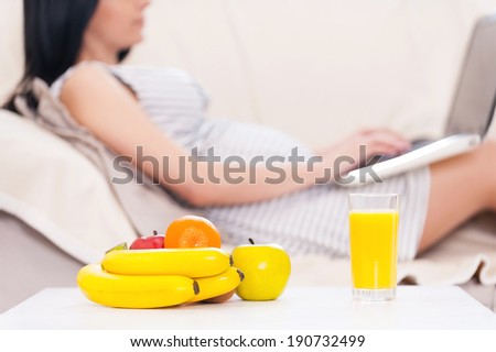 Pregnant woman with laptop. Beautiful pregnant woman working on laptop while lying on a couch