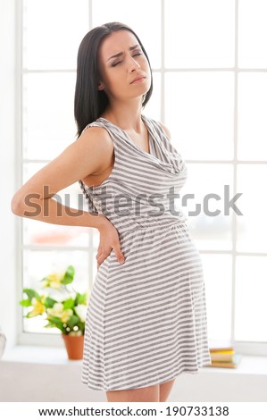 Pregnancy trials. Depressed pregnant woman holding hands on back and keeping eyes closed