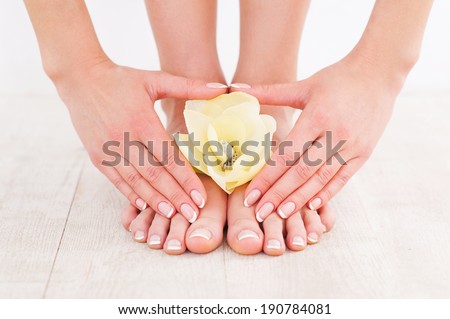 Beautiful manicure and pedicure. Close-up of young woman touching her feet while standing on hardwood floor