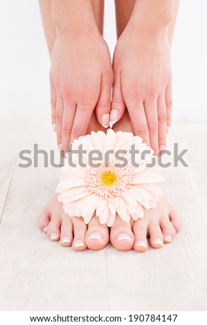 Beautiful feet. Close-up of young woman touching her feet while standing on hardwood floor