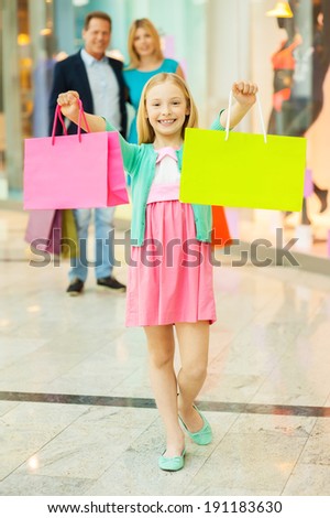 Family shopping. Cheerful family shopping in shopping mall while little girl showing her shopping bags and smiling