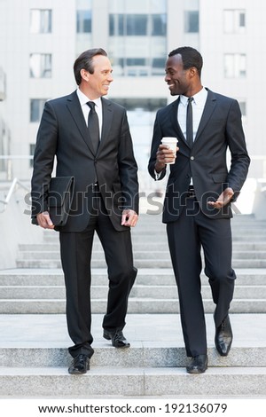 Business partners. Full length of two cheerful business men talking while moving down by staircase