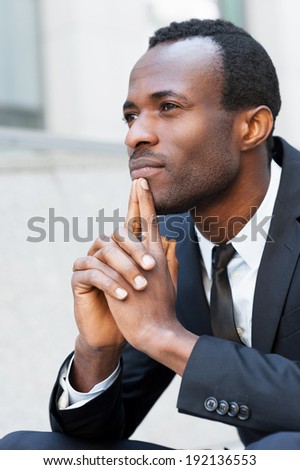 Lost in thoughts. Thoughtful young African man in formal wear keeping hands clasped and looking away while sitting outdoors