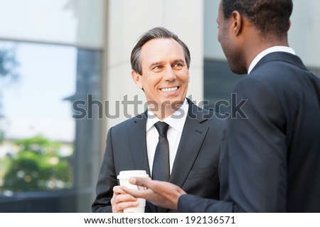 Having a coffee break to talk around. Two cheerful business men talking and gesturing while standing outdoors