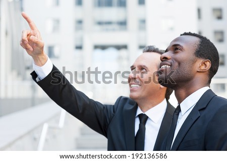 Look over there! Side view of two cheerful business men talking and gesturing while standing outdoors