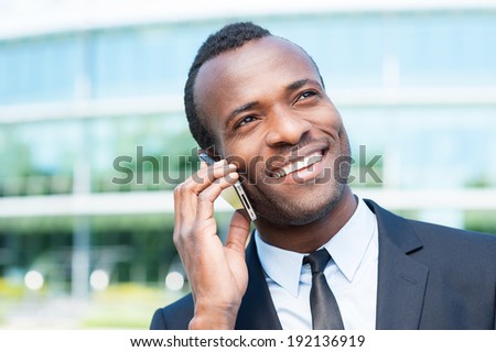 Business talk. Confident young African man in formal wear talking on the mobile phone and smiling while standing outdoors