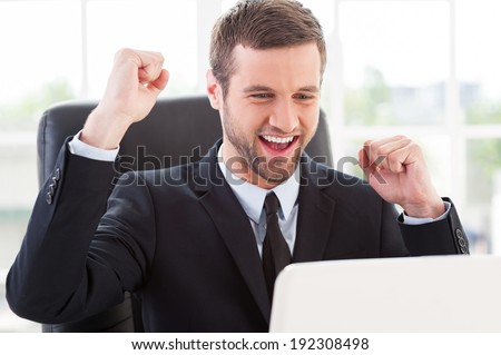 I did it! Happy young man in formal wear looking at computer monitor and gesturing while sitting at his working place