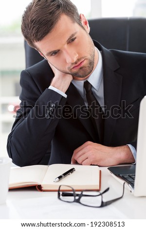 Tired businessman. Frustrated young man in formal wear looking away and touching his neck with hand while sitting at his working place