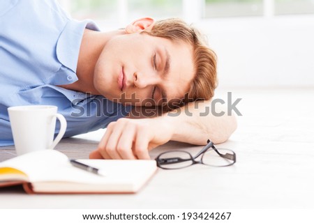 Tired and overworked. Handsome young man lying on the floor and keeping eyes closed