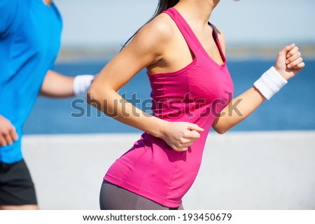 Jogging together.  Close-up of young woman and man in sports clothing running along the riverbank