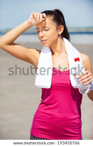 Relaxing after jog. Tired young woman drinking water and keeping eyes closed while standing outdoors