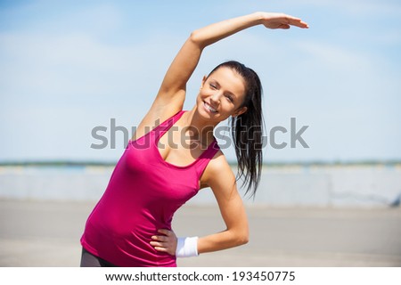 Doing stretching exercises. Beautiful young woman doing stretching exercises while standing outdoors