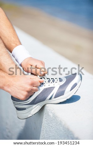 Tying shoelaces. Close-up of man tying shoelaces on sports shoe while standing outdoors