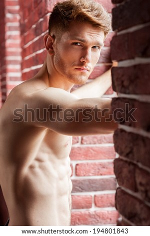 Feeling flirty. Handsome young shirtless man looking at camera while standing in front of the window