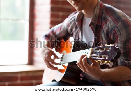 Playing guitar. Close-up of man playing acoustic guitar while sitting in front of the window