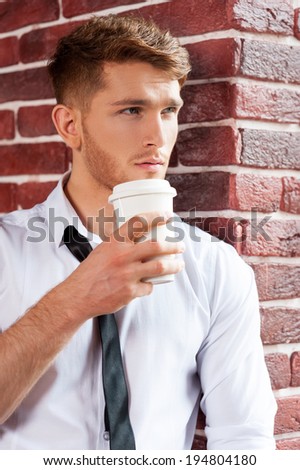 Waiting for inspiration. Handsome young man in shirt and tie holding coffee cup and looking through the window