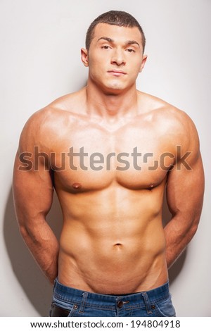 Strong and muscular. Confident young shirtless man looking at camera while standing against grey background
