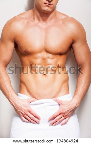 Perfect male body. Close-up of young shirtless man covered with towel standing against background