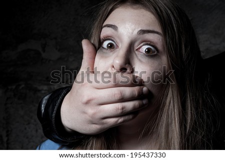 Kidnapping. Terrified young woman with hand covering her mouth staring at camera