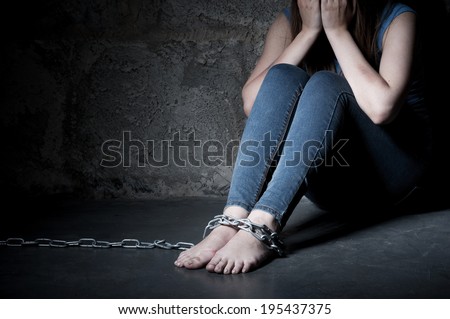 Trapped woman. Young woman trapped in chains covering face with hands while sitting on the floor in a dark room