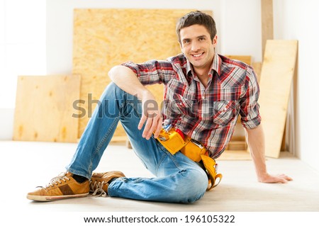 Handyman relaxing. Handsome young handyman in talking on the mobile phone and smiling while sitting on the floor
