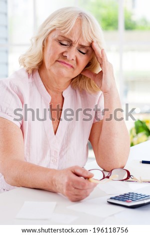 Financial problems. Frustrated senior woman leaning her head on hand and keeping eyes closed while sitting at the table with bills and calculator on it