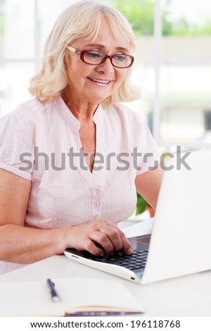 Working at home. Happy senior woman working at the laptop and smiling while sitting at the table
