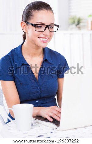 Surfing the net in cafe. Beautiful young woman working on laptop and smiling while sitting in cafe