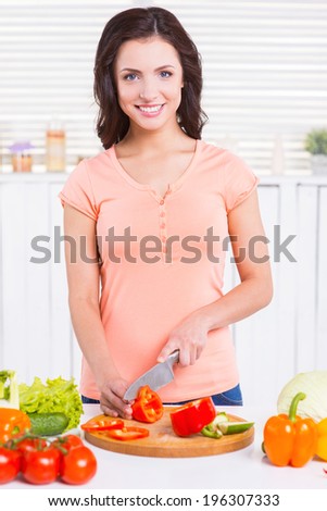 Preparing her favorite salad. Attractive young woman cutting vegetables on cutting board and smiling while standing on the kitchen