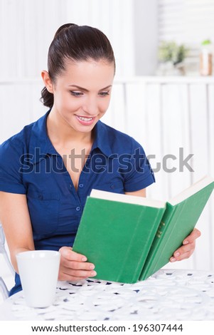 Reading her favorite book in cafe. Beautiful young woman reading book and smiling while sitting in cafe