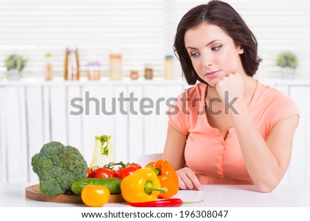 What to cook? Beautiful young woman holding hand on chin and looking at the vegetables laying on the table