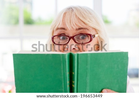So exciting book! Surprised senior woman holding a book and looking out of it