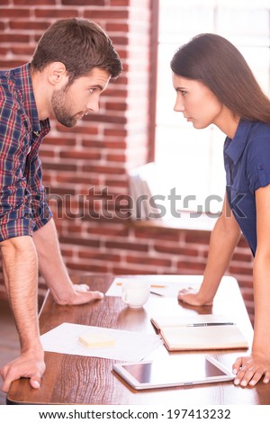 Business confrontation. Side view image of angry man and woman standing face to face while leaning at the office table
