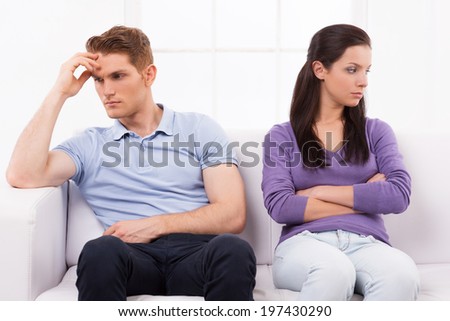 A huge rift in their relationship. Depressed young man and woman sitting close to each other on the couch and looking away