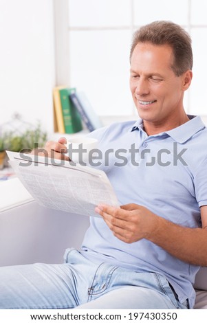 Relaxing with fresh coffee and latest news. Cheerful mature man drinking coffee and reading newspaper while sitting on the couch at home