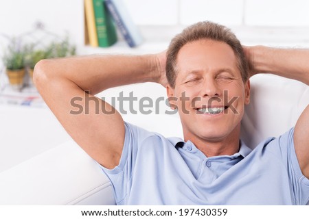 Total relaxation. Happy mature man lying on the couch and keeping hands behind head