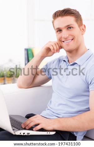 Surfing the net at home. Handsome young man sitting on the couch and working on laptop