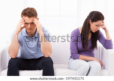 Relationship difficulties. Depressed young man and woman sitting close to each other on the couch and holding head in hands