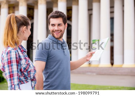 Follow me! Happy young tourist couple walking near beautiful building while man holding map