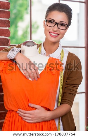 Beautiful fashion designer. Beautiful young female fashion designer embracing mannequin in orange dress and smiling