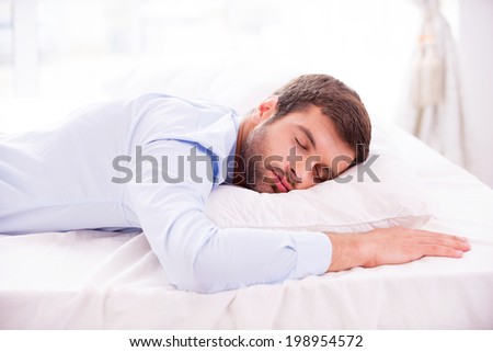 Tired and overworked. Handsome young man in shirt sleeping in bed