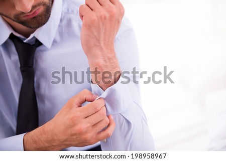 Adjusting shirt sleeves. Close-up of man in blue shirt adjusting sleeve while sitting on the sofa