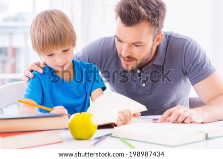 Helping son with homework. Confident young father helping his son with homework while sitting at the table together